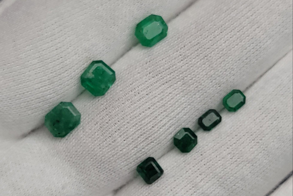 Five green faceted gemstone beads of varying sizes displayed on a white textured glove.