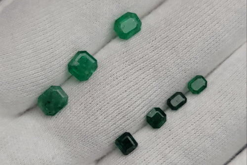 Five green faceted gemstone beads of varying sizes displayed on a white textured glove.