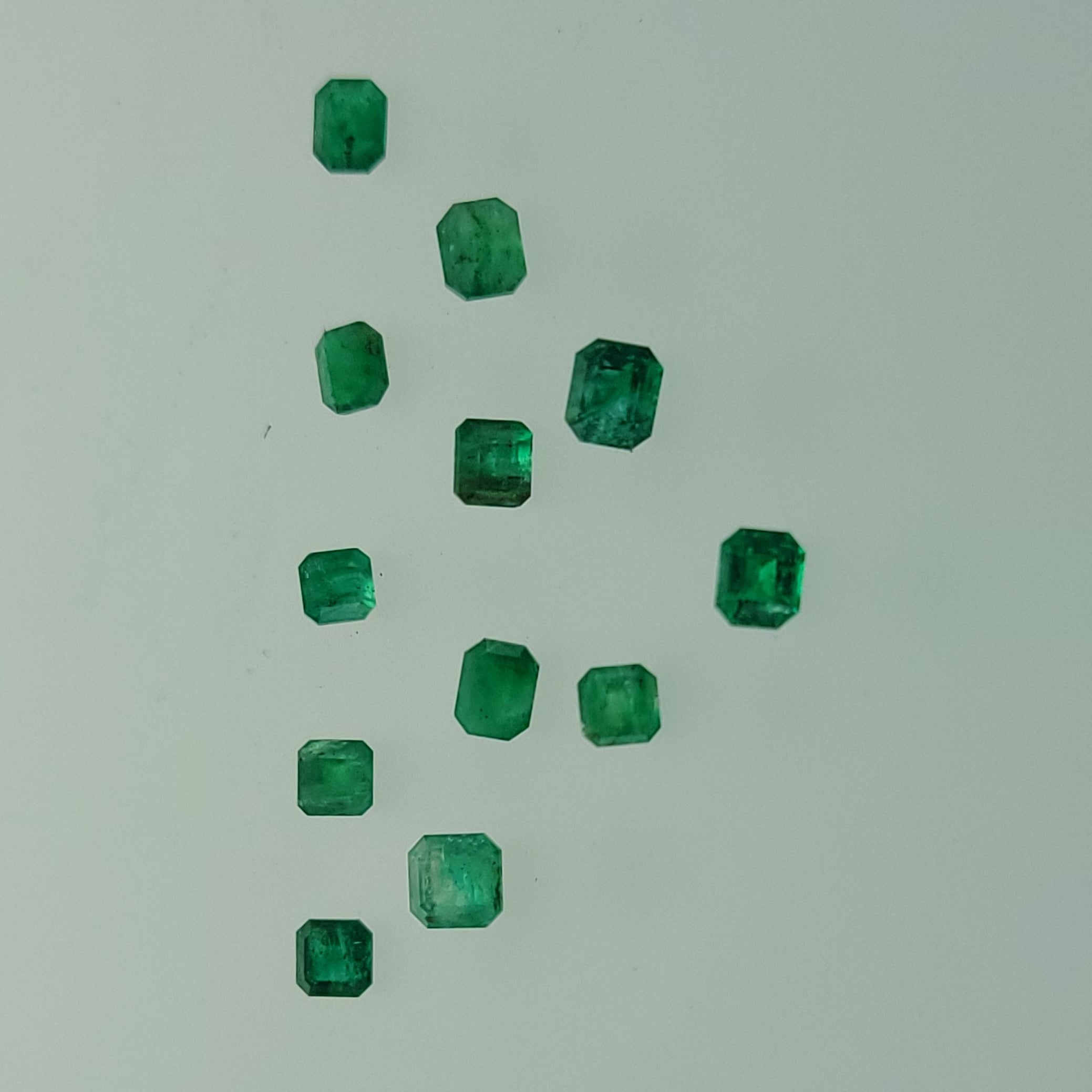 Ten small green emerald-cut gemstones arranged in a loose triangular cluster on a plain light gray background.
