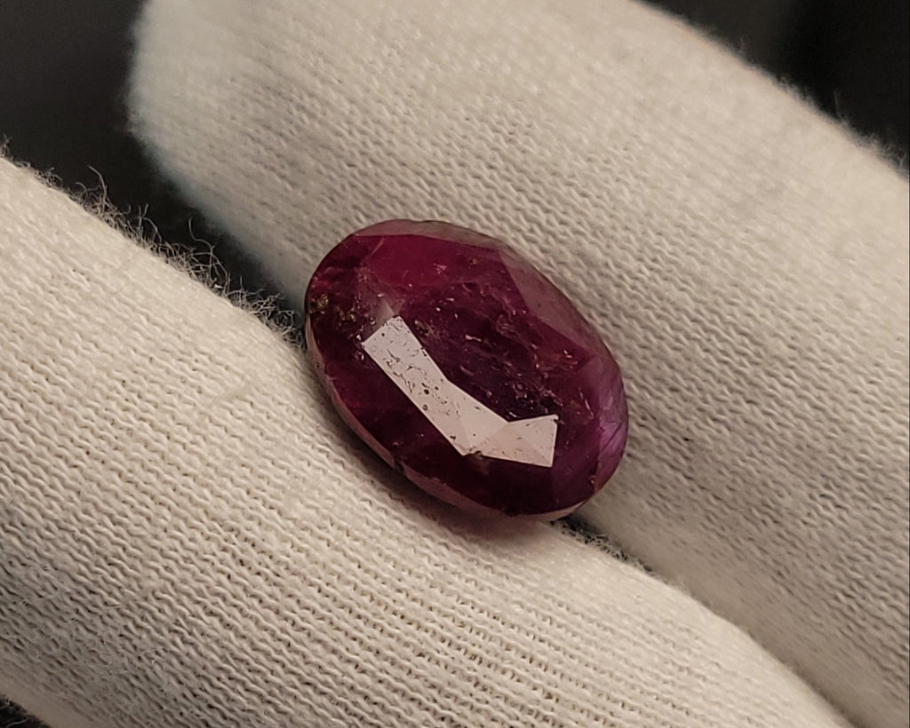 A small oval deep pinkish-red gemstone resting on a white textured fabric glove.