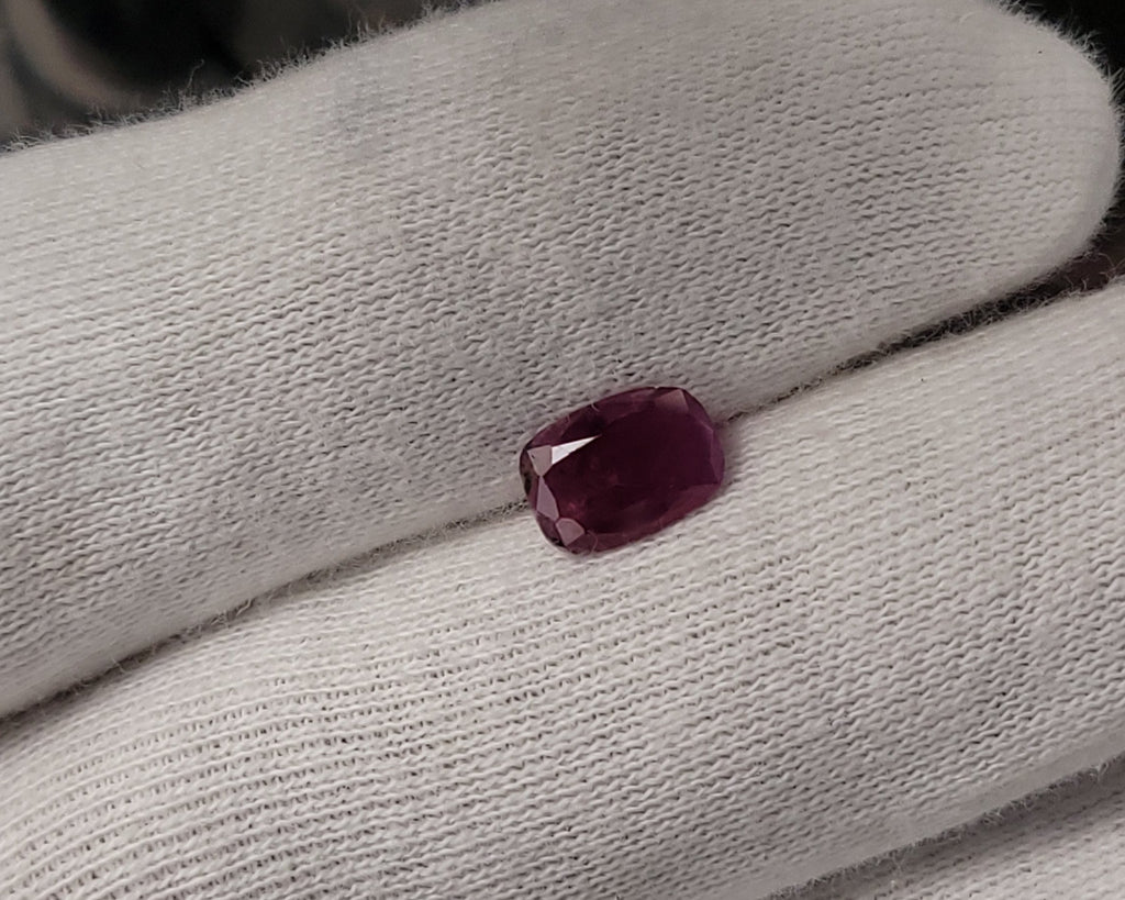 A small rectangular faceted dark purple gemstone resting on a white knit glove.