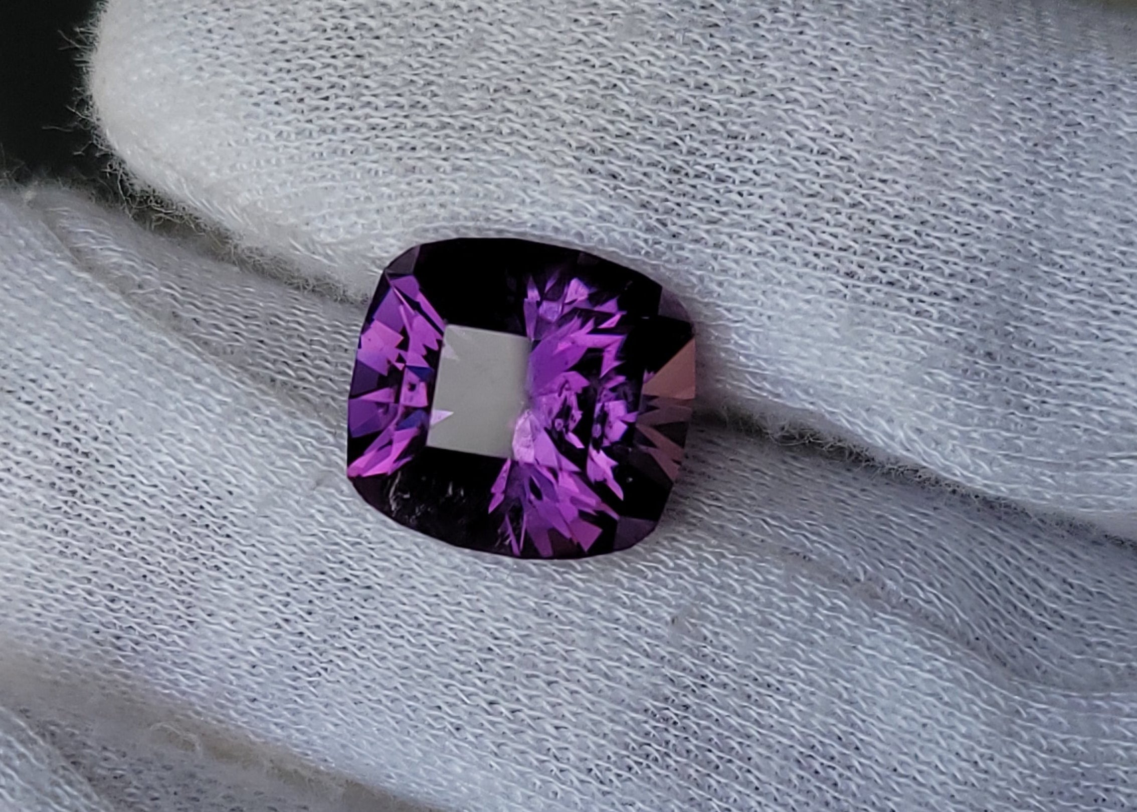 A cushion-cut purple gemstone with a white center, held on a white knit glove.