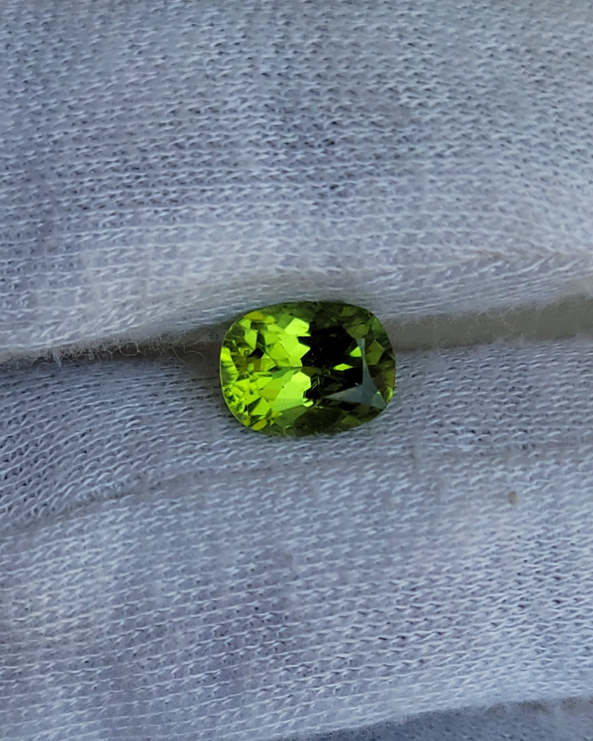 A small oval-cut green gemstone resting on a textured white fabric surface.