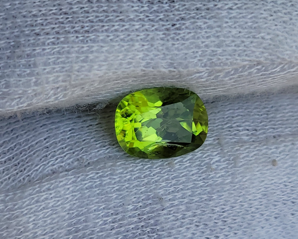 A small oval-cut green gemstone resting on a textured white fabric surface.
