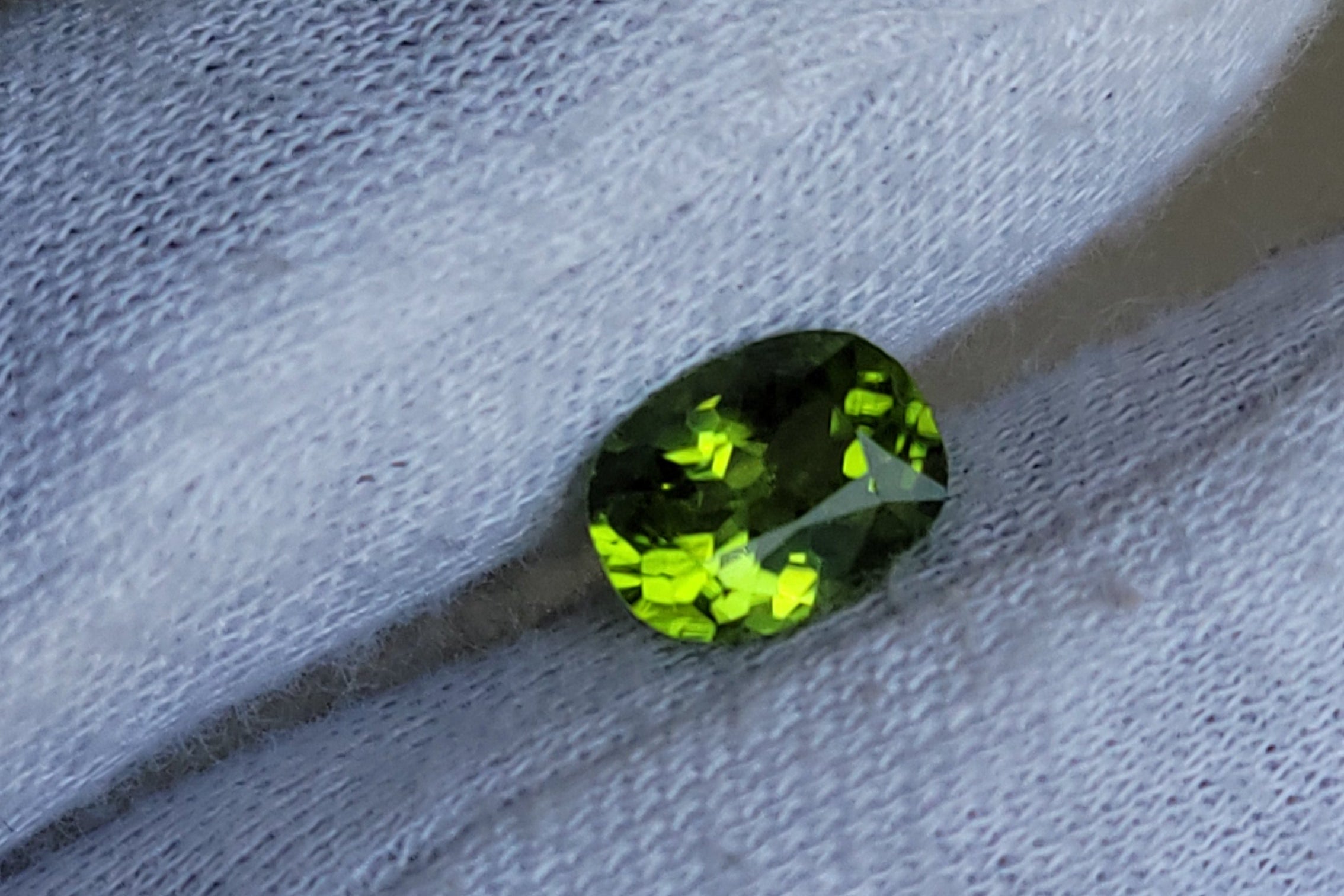 A small oval green gemstone resting on a white textured fabric surface.