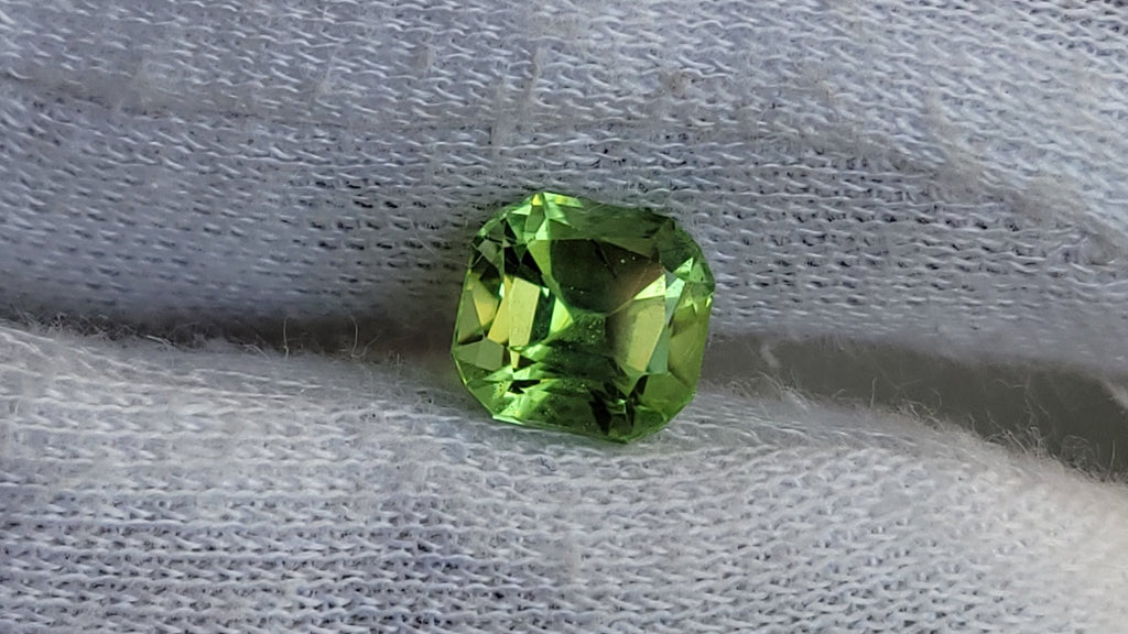 A small round green gemstone held against a white knit-gloved hand.