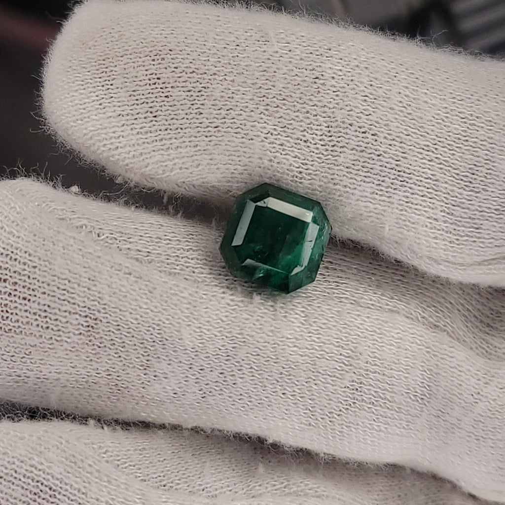 A small green faceted gemstone held on a white textured fabric glove.