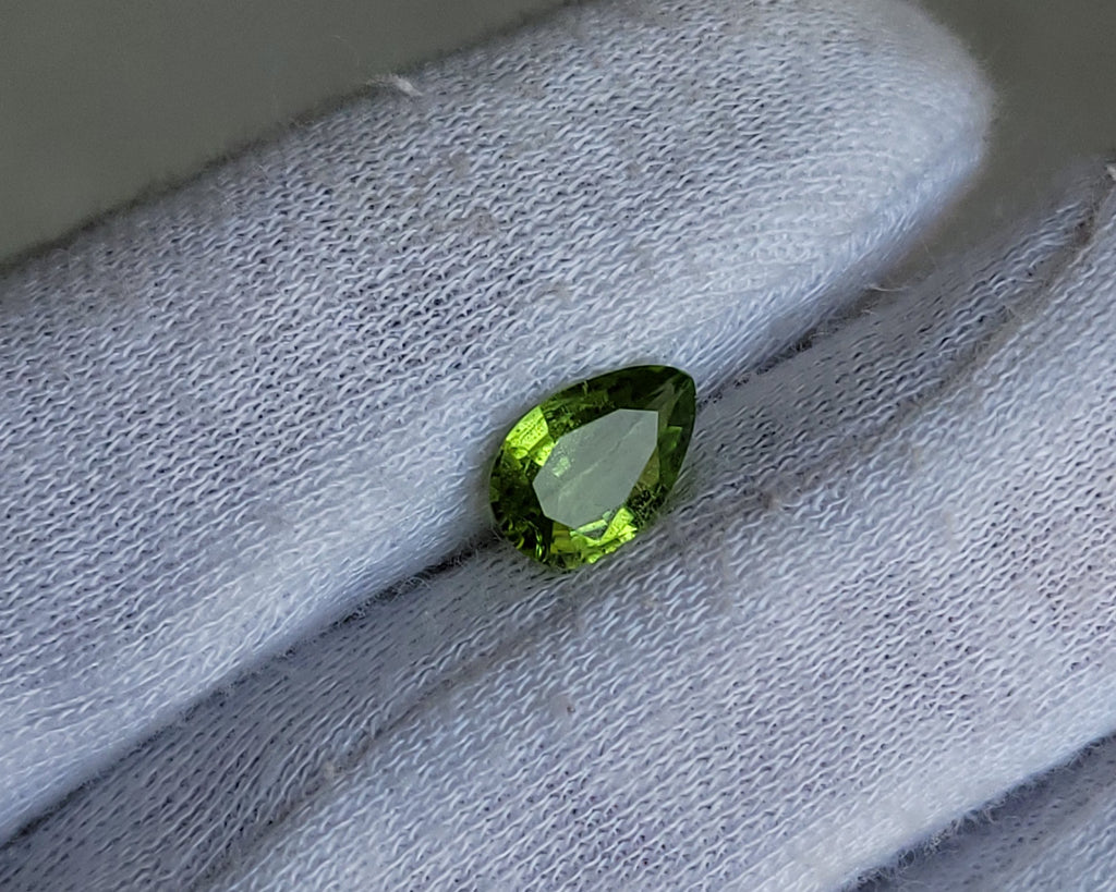 A small pear-cut green gemstone held on a white gloved finger.