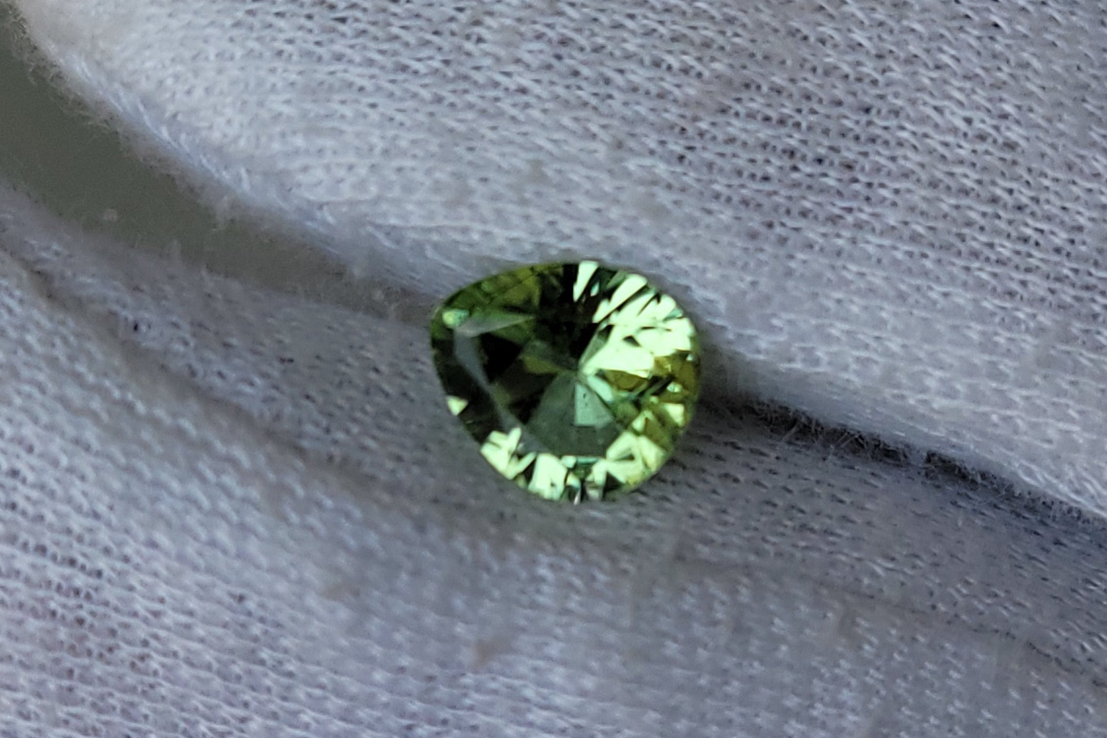 A small round green gemstone held on a white textured fabric-covered finger.