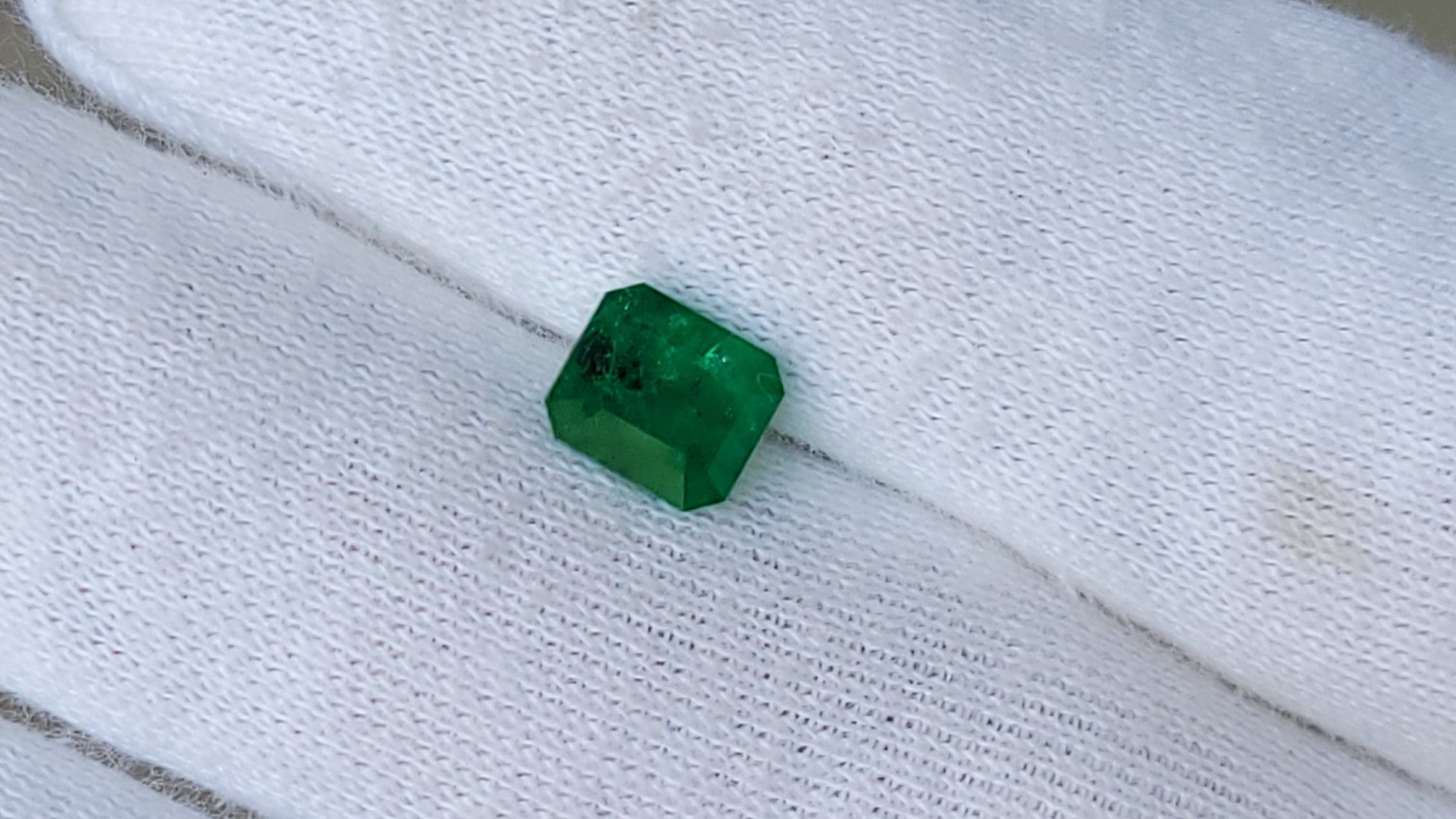 A small green rectangular gemstone held on a white gloved hand.