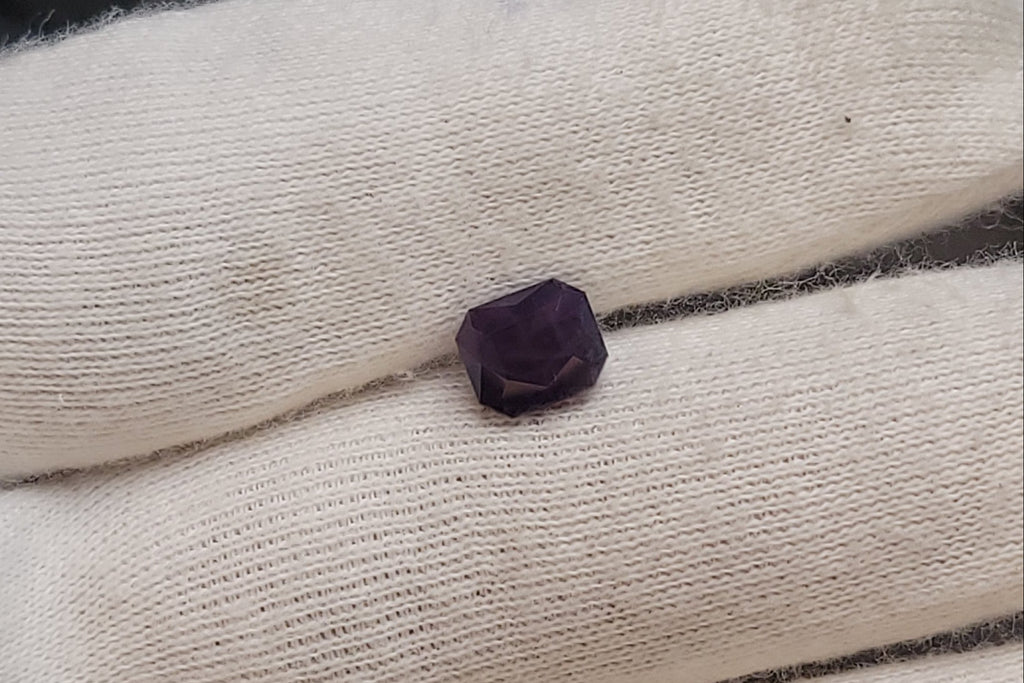 A small dark purple gemstone or bead resting on a white knit glove, photographed close up.