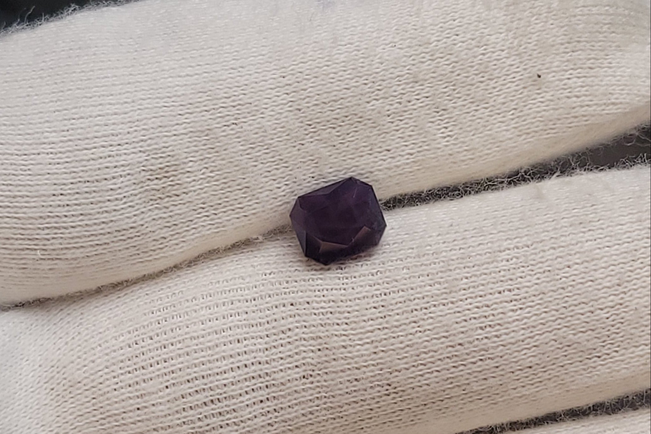 A small dark purple gemstone or bead resting on a white knit glove, photographed close up.