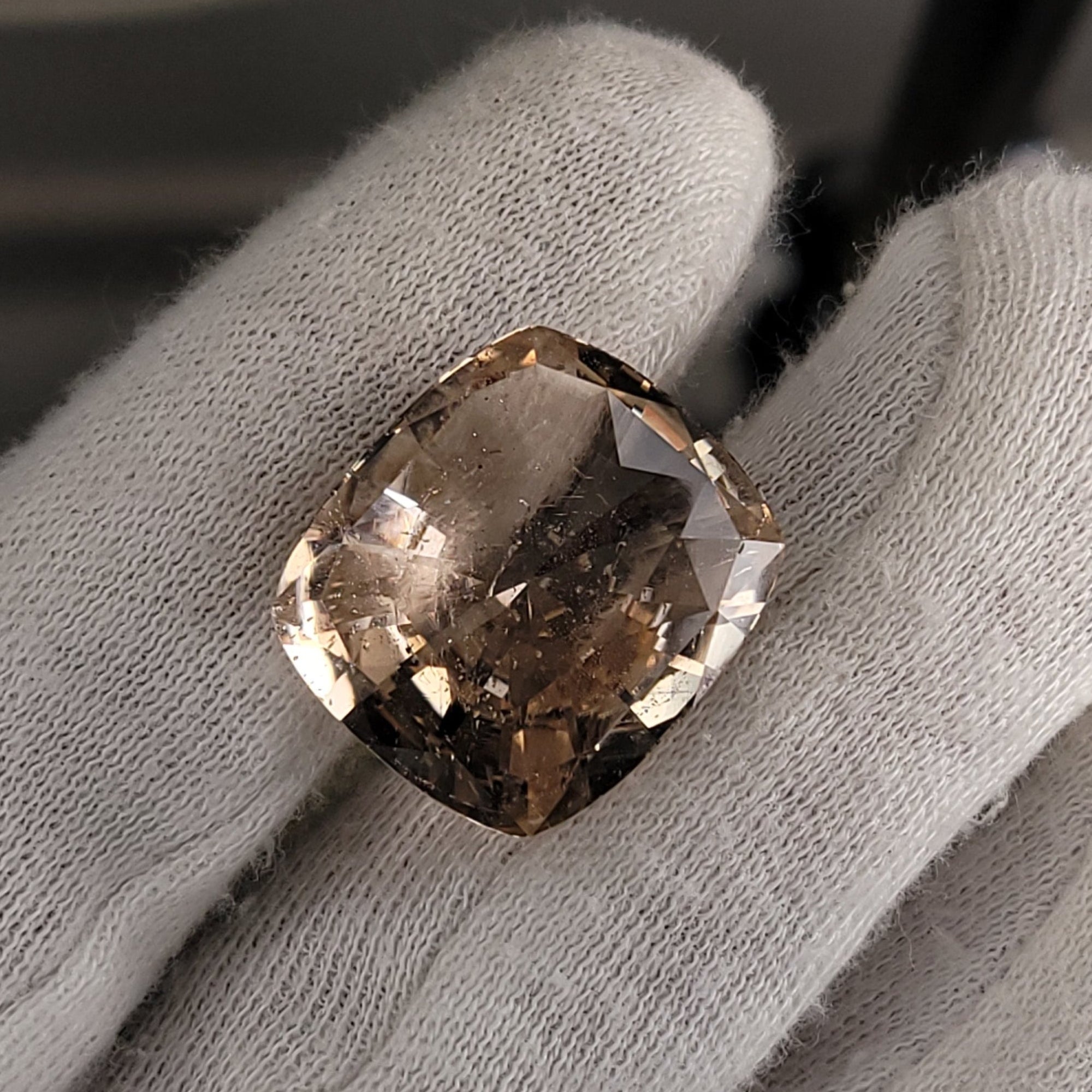 A cushion-cut, square-shaped champagne-colored gemstone held between white cotton gloves.