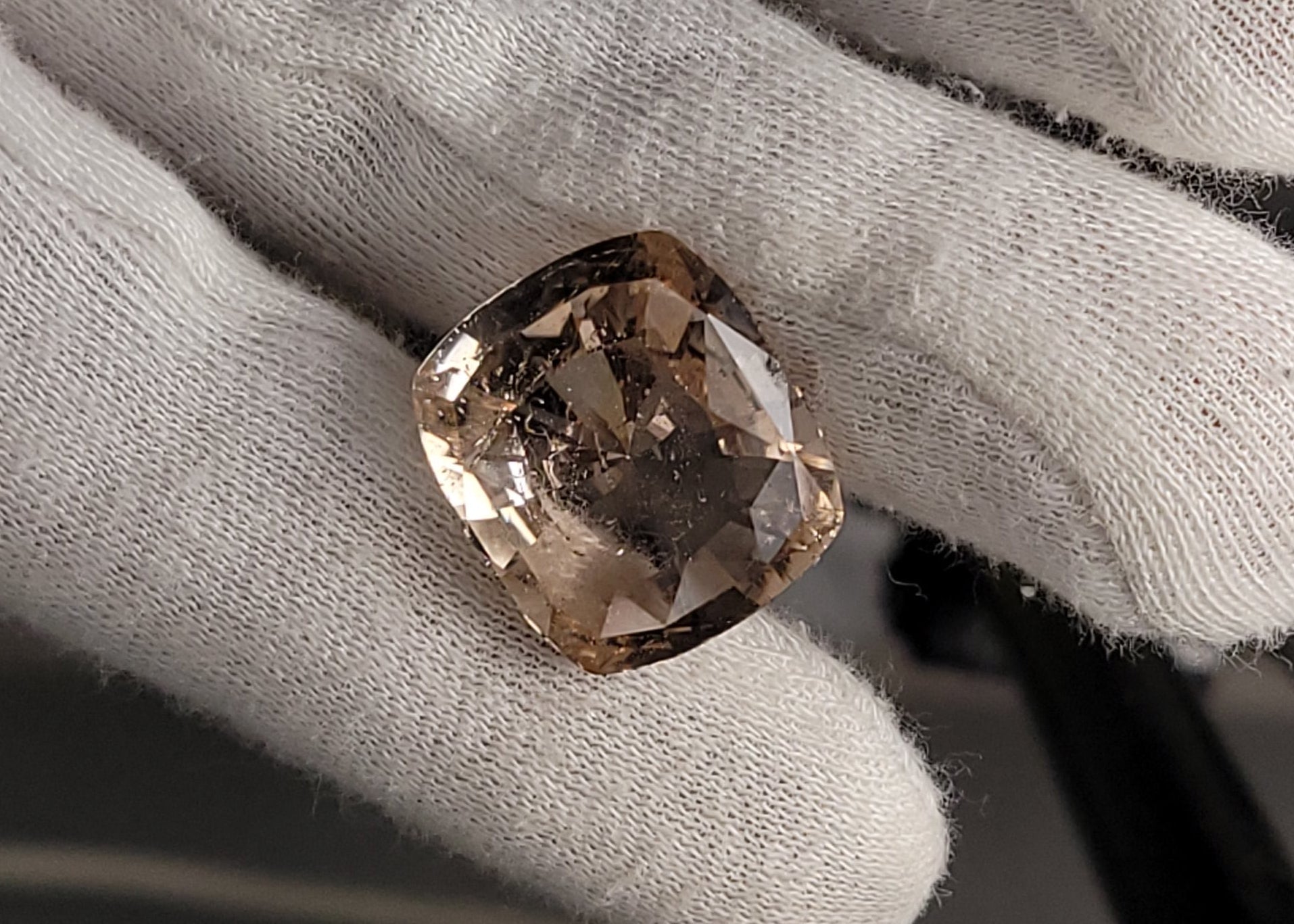 A cushion-cut pale pinkish-brown gemstone held on a person's gloved hand.