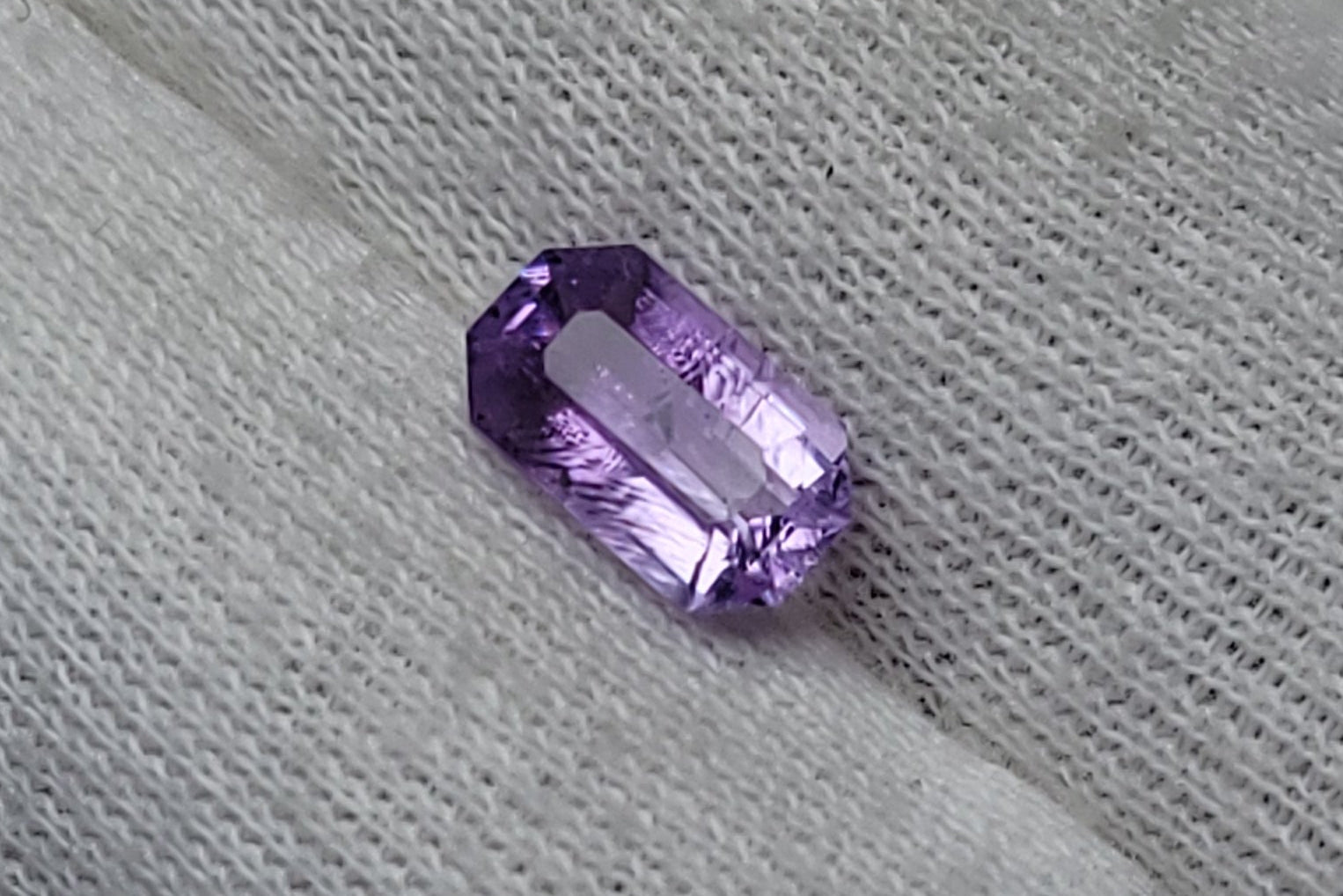 A small oval-cut purple gemstone resting on a white textured fabric glove.