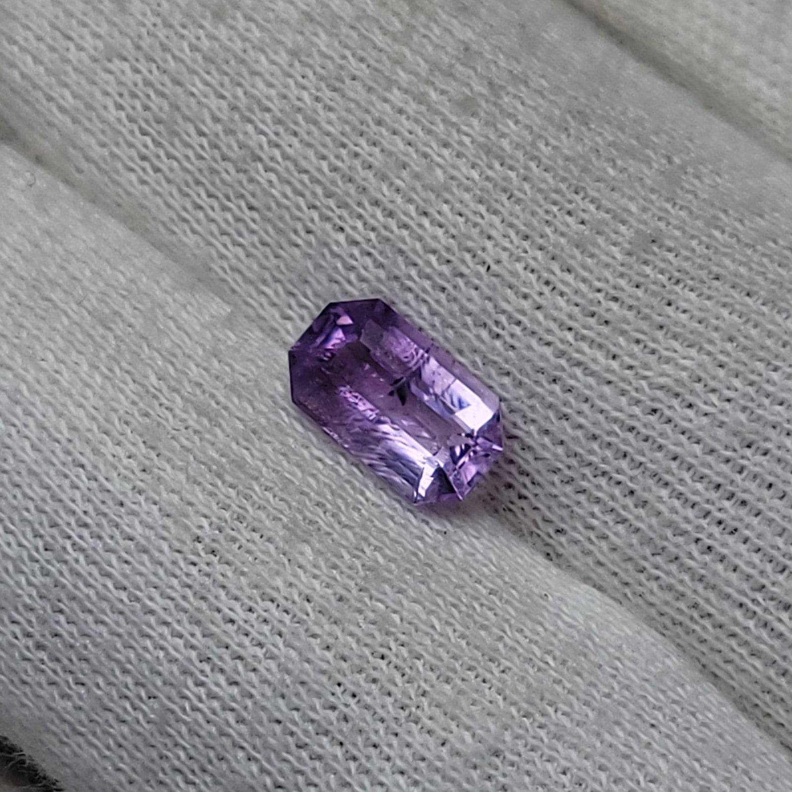 A small rectangular purple gemstone resting on a white textured fabric-covered finger.