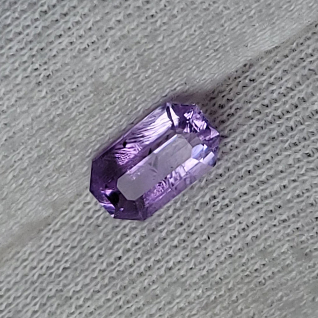 A small rectangular purple gemstone held on the fingers of a hand wearing a white knit glove.