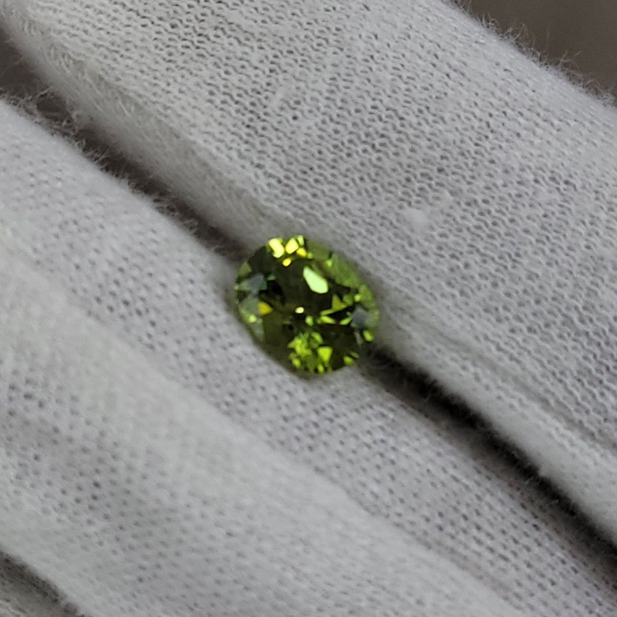 A small oval-cut green gemstone displayed on a white textured fabric surface.