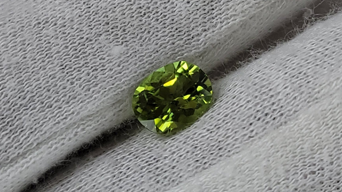 A small oval-cut green gemstone displayed on a white textured fabric glove.