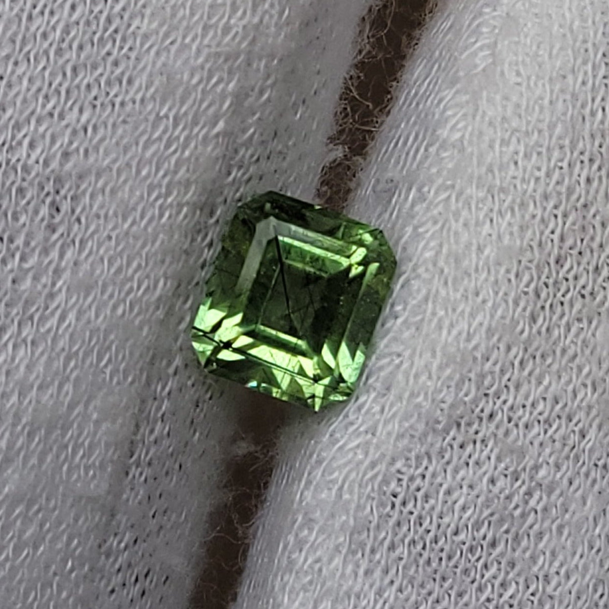 A small rectangular green gemstone held on a white gloved finger against a plain neutral background.