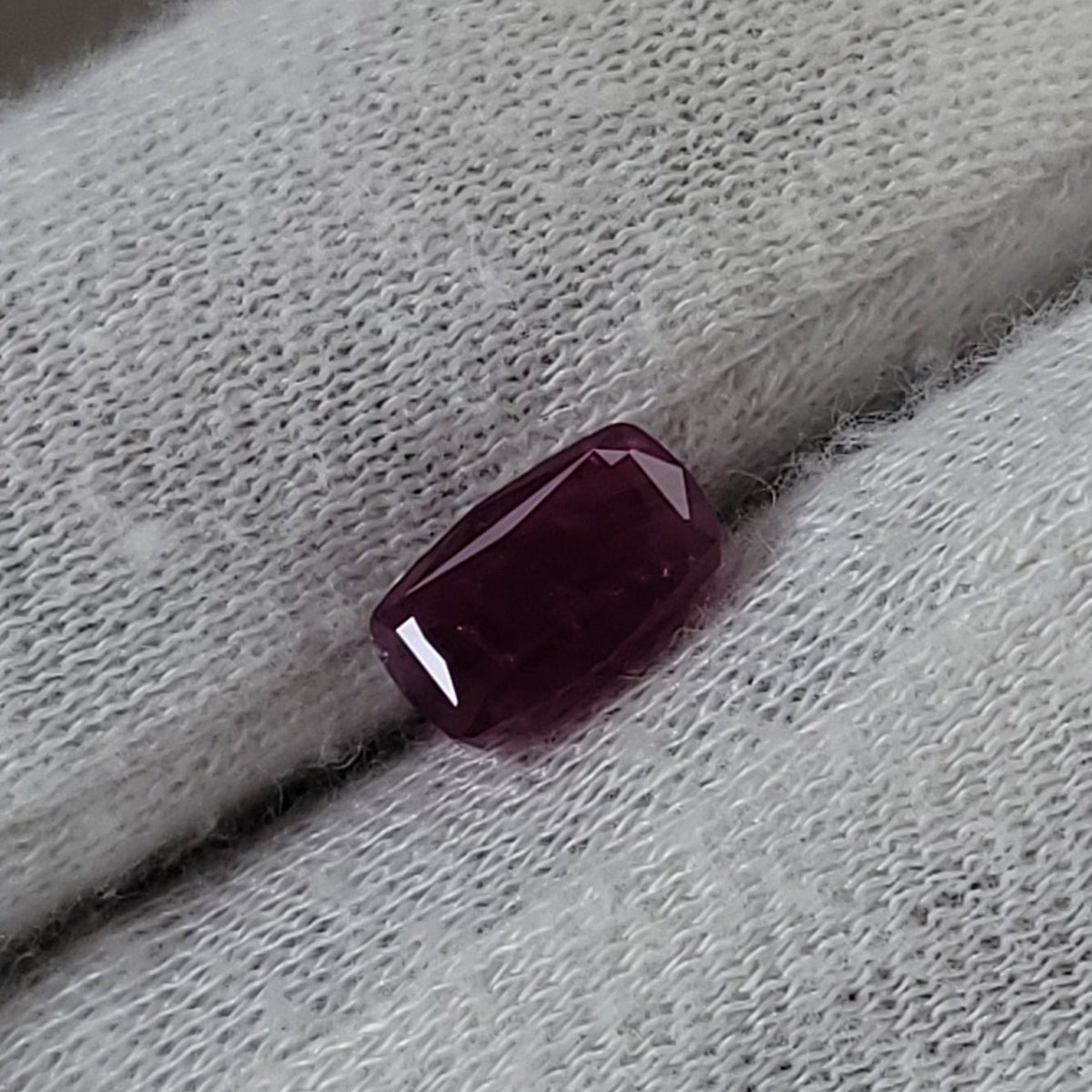 A small rectangular dark red gemstone or bead resting on a white knit fabric surface.