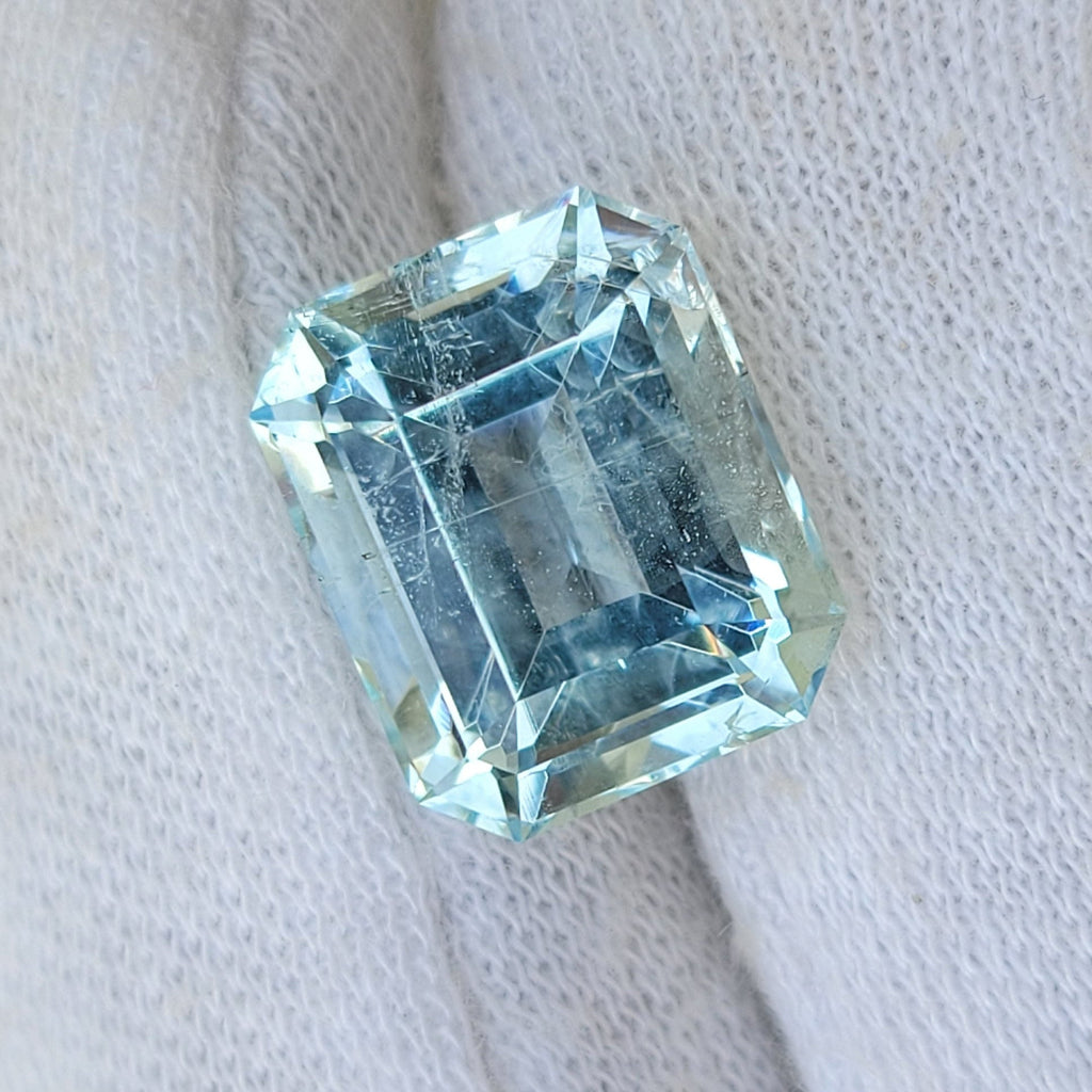 A light blue emerald-cut gemstone displayed on a white knit gloved finger.