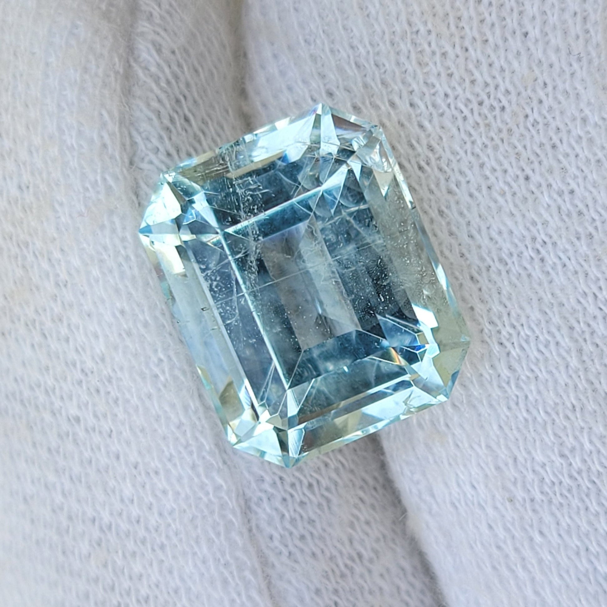 A light blue emerald-cut gemstone displayed on a white knit gloved finger.