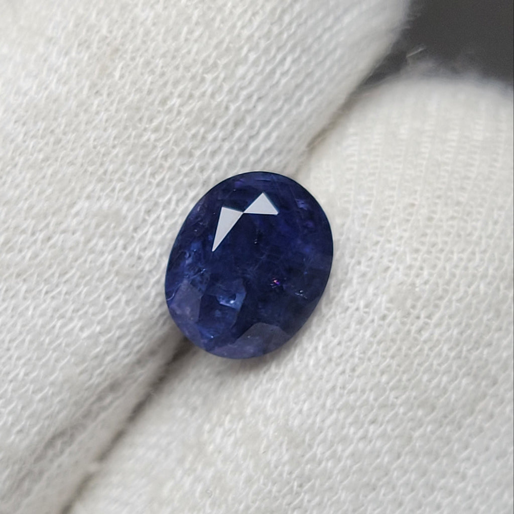 A small oval-cut deep blue gemstone resting on white textured fabric.