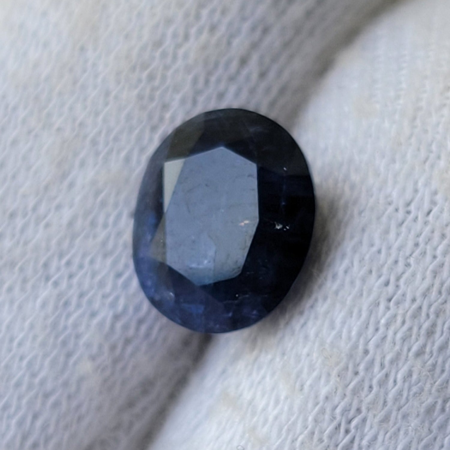 A small oval dark blue gemstone held on a white textured glove.