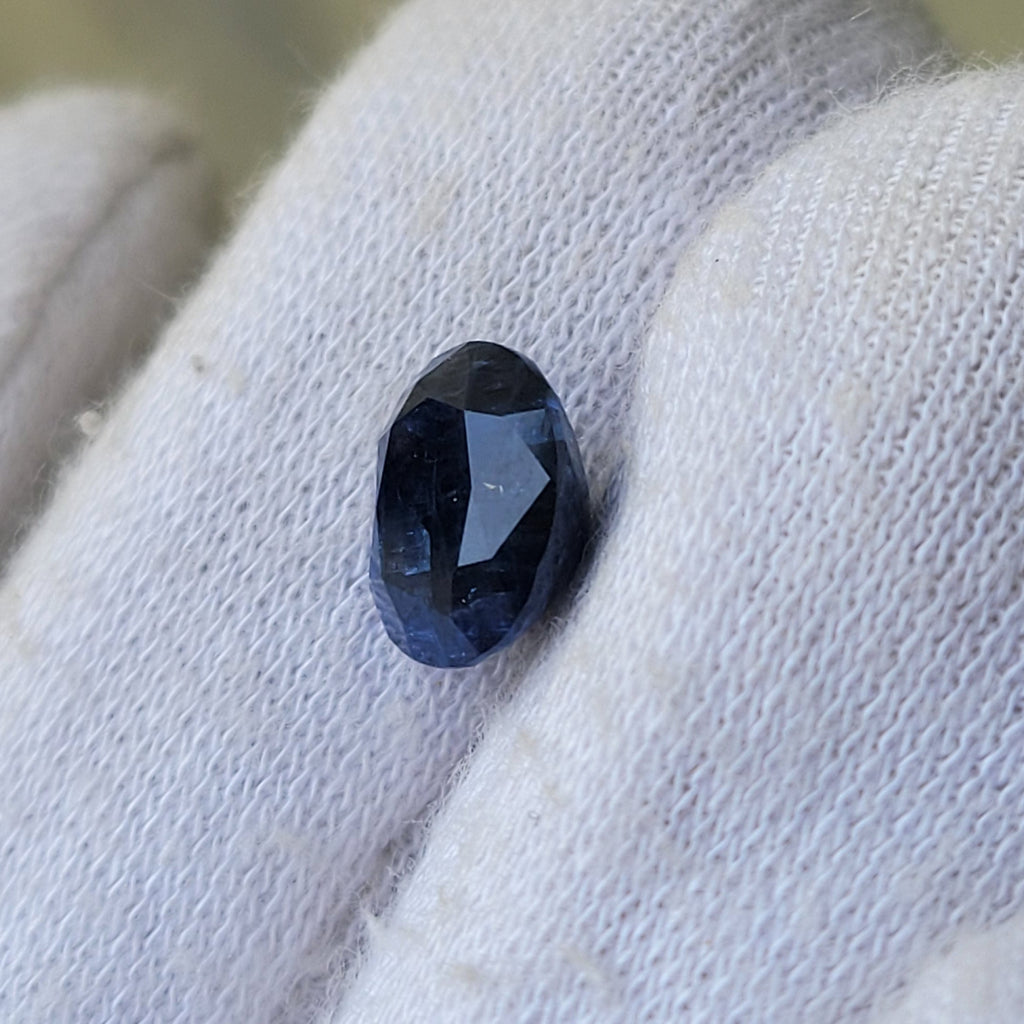 A small oval dark blue gemstone held on a white knitted gloved finger.