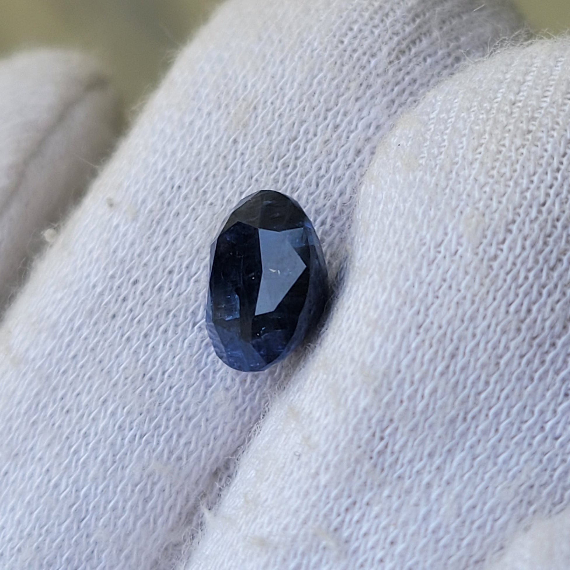 A small oval dark blue gemstone held on a white knitted gloved finger.
