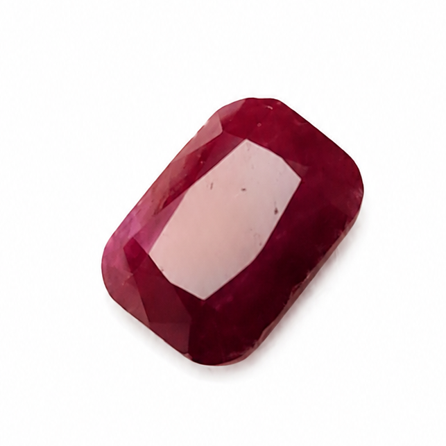 A single rectangular cabochon-cut ruby gemstone with a faceted center, showing a deep red color and a light pink internal reflection, set against a plain white background.