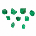 Seven raw green emerald crystals of varying sizes arranged on a plain white background.