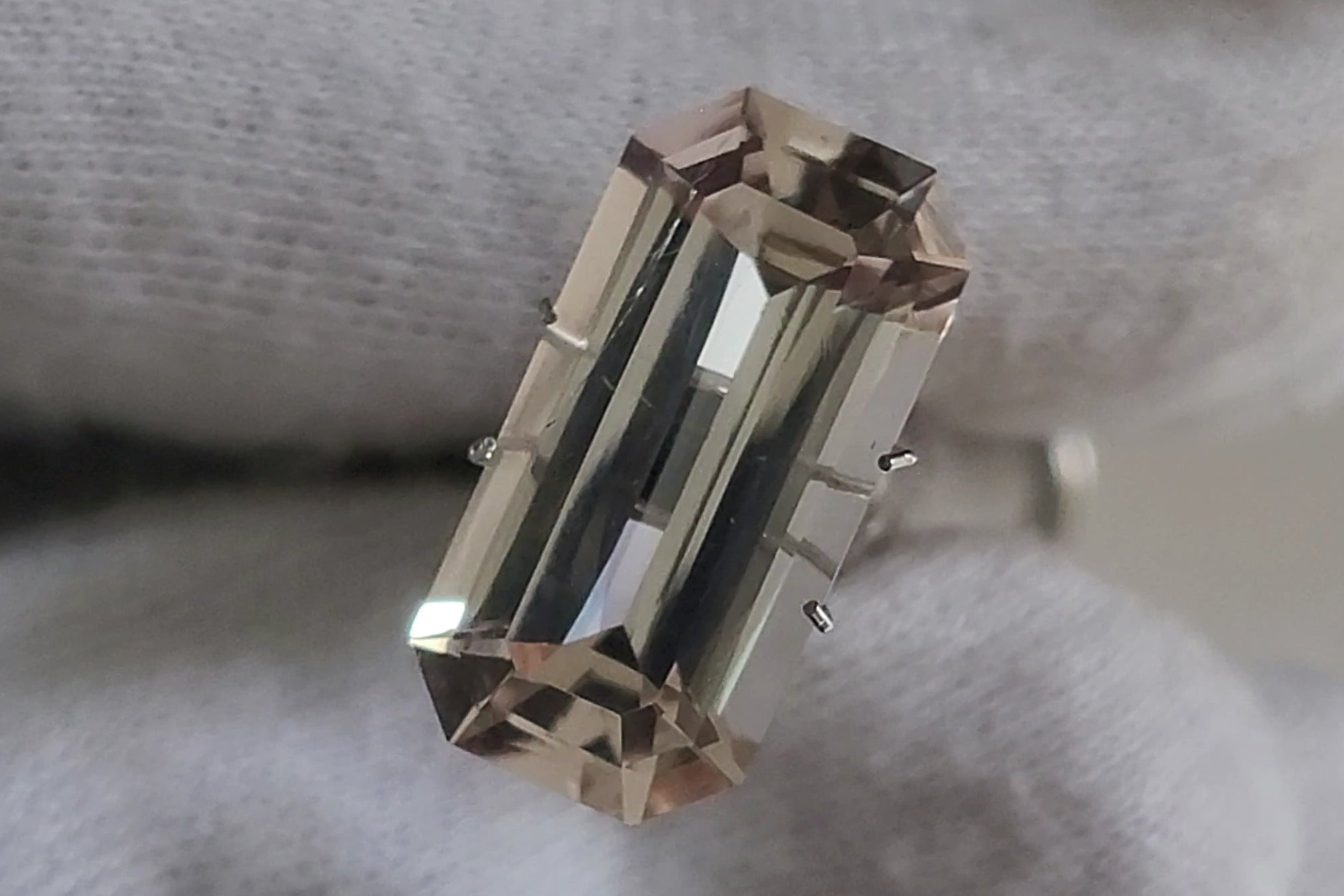 A rectangular baguette-cut clear gemstone ring set in silver-toned metal, held by a hand wearing a white textured glove.