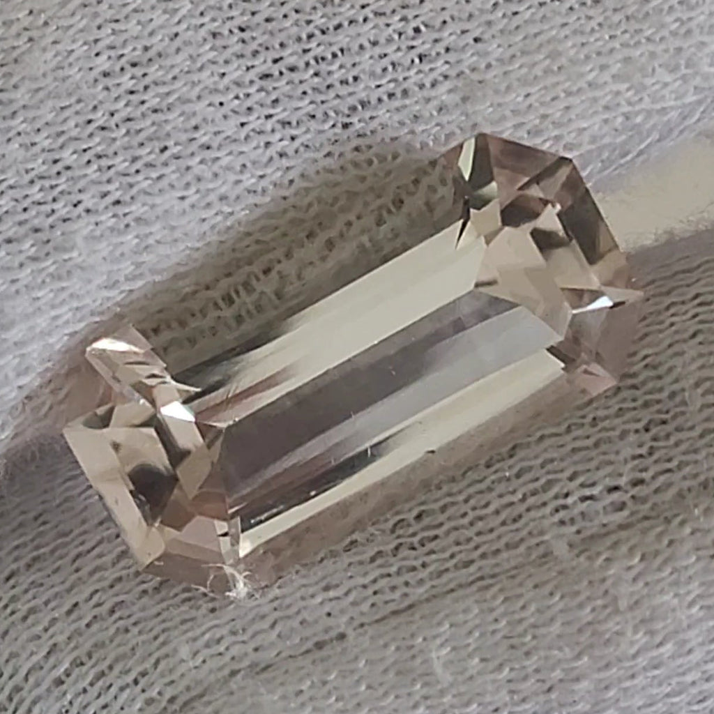 A rectangular clear gemstone with faceted edges, held on a white textured fabric-covered finger.